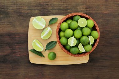 Whole and cut fresh ripe limes in bowl on wooden table, top view