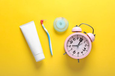 Container with dental floss, toothpaste and toothbrush on yellow background, flat lay