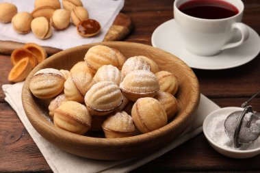 Delicious nut shaped cookies with boiled condensed milk and powdered sugar on wooden table, closeup