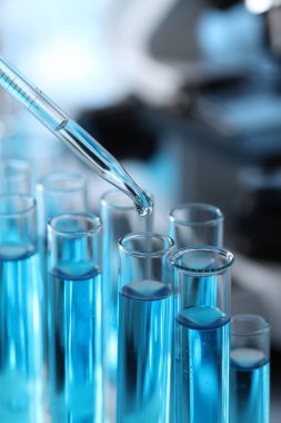 Dripping liquid from pipette into test tube in laboratory, closeup