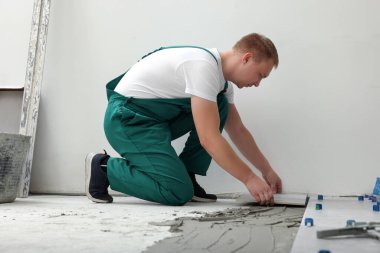Worker installing ceramic tile on floor near wall