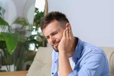Young man suffering from ear pain at home. Space for text