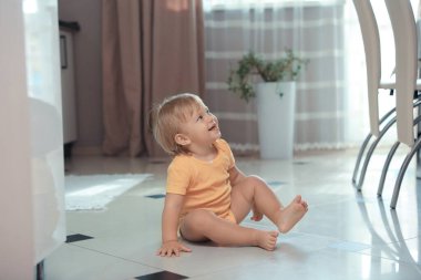 Cute baby sitting on floor in room. Learning to walk