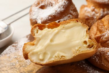 Delicious profiteroles with cream filling inside on wooden table, closeup