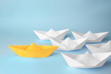 Group of paper boats following yellow one on light blue background. Leadership concept