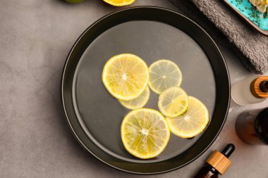 Flat lay composition with essential oil and lemons on grey table. Aromatherapy treatment