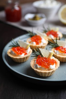 Delicious tartlets with red caviar and cream cheese served on wooden table, closeup