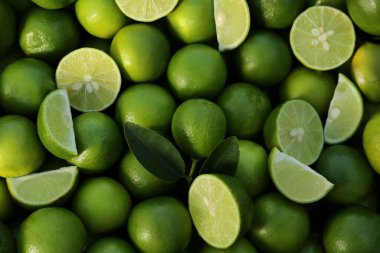 Whole and cut fresh ripe green limes as background, closeup view