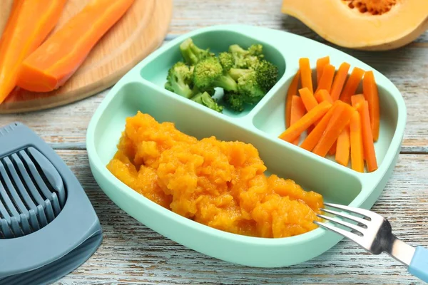 Baby food. Section plate with vegetables and pumpkin puree served on rustic wooden table, closeup