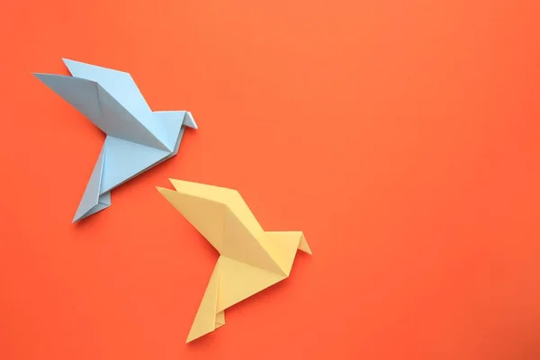 Beautiful colorful origami birds on orange background, flat lay. Space for text