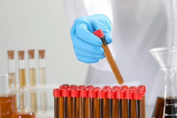 Scientist taking test tube with brown liquid from stand, closeup