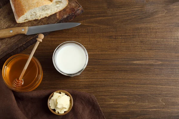 Flat lay composition of honey, milk and butter on wooden table. Space for text