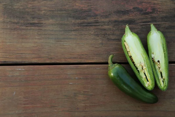Whole and cut green chili peppers on wooden table, flat lay. Space for text