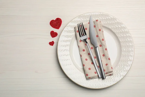 Plate with cutlery and decorative hearts on white wooden table for romantic dinner, top view. Space for text