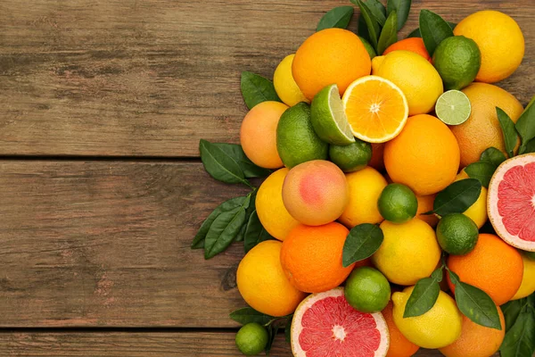 stock image Different citrus fruits with green leaves on wooden table, flat lay. Space for text