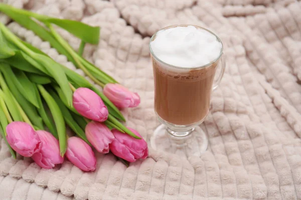 Glass of delicious cocoa and pink tulips on light blanket