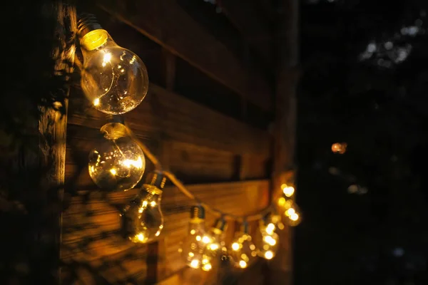 Garland of lamp bulbs hanging on wooden wall, space for text. String lights