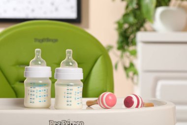 High chair with feeding bottles of infant formula and toy maracas on white tray indoors