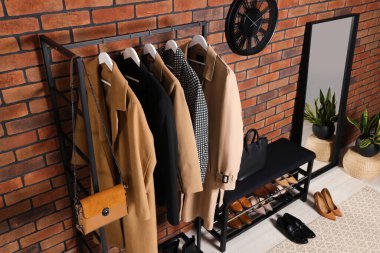 Stylish hallway with coat rack and shoe storage bench near brick wall. Interior design