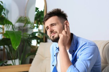 Young man suffering from ear pain at home. Space for text