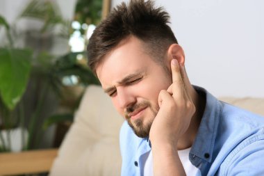 Young man suffering from ear pain at home. Space for text