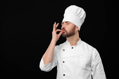 Mature chef showing delicious gesture on black background, space for text
