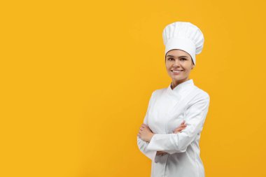 Happy female chef wearing uniform and cap on orange background. Space for text