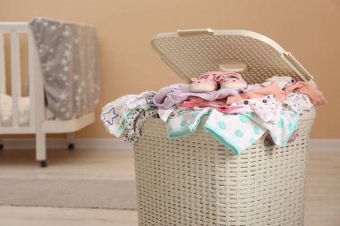 Laundry basket with baby clothes in child room, space for text