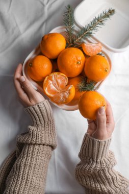 Woman with delicious ripe tangerines on white bedsheet, top view