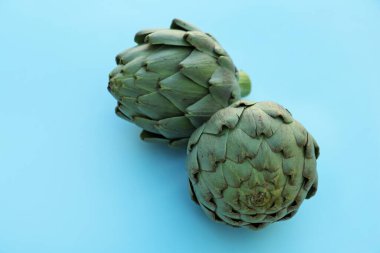 Whole fresh raw artichokes on light blue background, closeup
