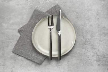 Clean plate with shiny silver cutlery on light grey table, flat lay