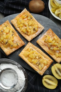 Fresh tasty puff pastry with sugar powder and kiwi served on grey table, flat lay