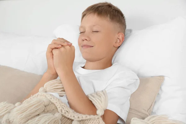 Boy with clasped hands praying in bed