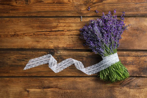 Beautiful fresh lavender bouquet with lace ribbon on wooden background, top view