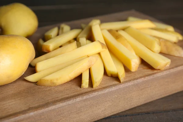 Whole and cut raw potatoes on wooden table, closeup. Cooking delicious French fries