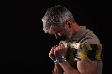 Victim tied with duct tape on black background, space for text. Hostage taking