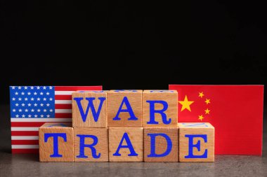 Words War Trade made of wooden cubes, American and Chinese flags on grey table against black background