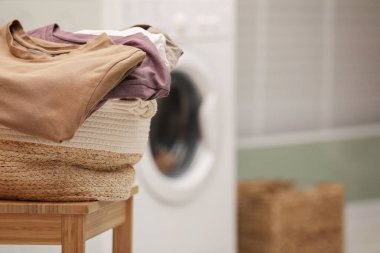 Laundry basket filled with clothes on chair in bathroom, closeup. Space for text