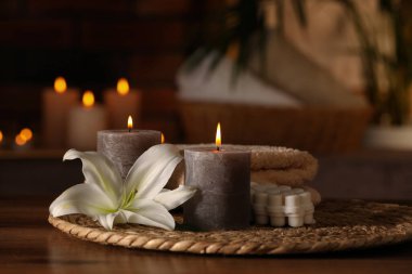 Spa composition with burning candles, lily flower and towels on wooden table in wellness center