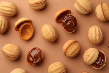 Homemade walnut shaped cookies with boiled condensed milk on pale brown background, flat lay