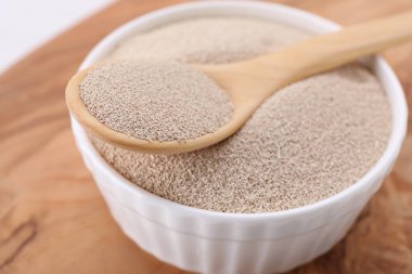 Bowl and spoon with active dry yeast on wooden board, closeup