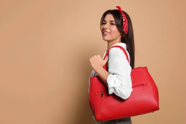 Young woman with stylish bag on beige background, space for text