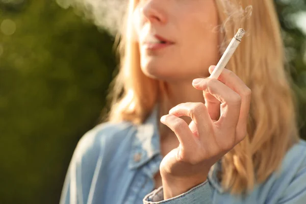 Young woman smoking cigarette outdoors, closeup view