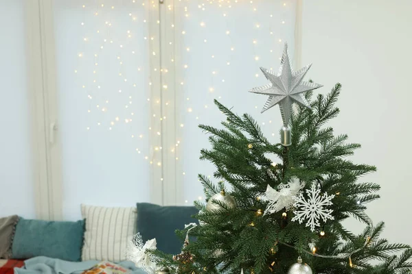 Interior design. Beautiful Christmas tree near cozy window sill and festive lights in room, space for text