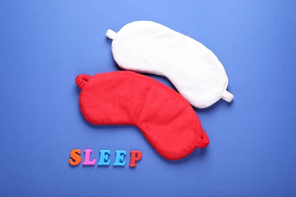Soft sleep masks and word Sleep made of colorful letters on blue background, flat lay