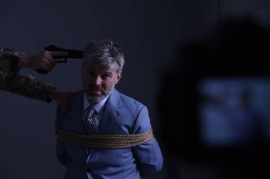 Kidnapper aiming gun at tied victim on dark background, space for text. Hostage taking