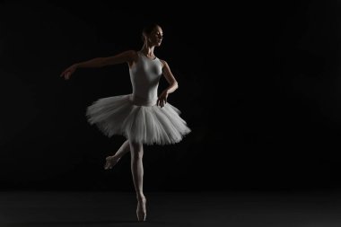 Young ballerina practicing dance moves on black background. Space for text