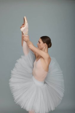 Young ballerina practicing dance moves on light grey background