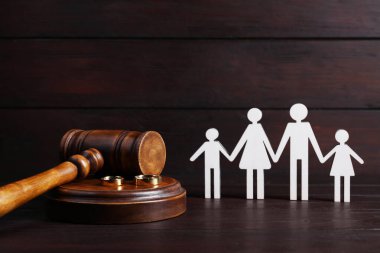 Divorce concept. Gavel, wedding rings and paper cutout of family on wooden table