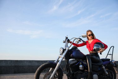 Beautiful young woman with helmet sitting on motorcycle outdoors